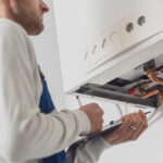 Professional,Plumber,Servicing,A,Boiler,And,Writing,On,A,Clipboard