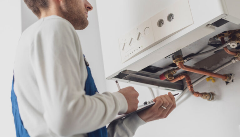 Professional,Plumber,Servicing,A,Boiler,And,Writing,On,A,Clipboard