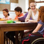 Primary school teacher helping child with special educational needs classroom UK landscape
